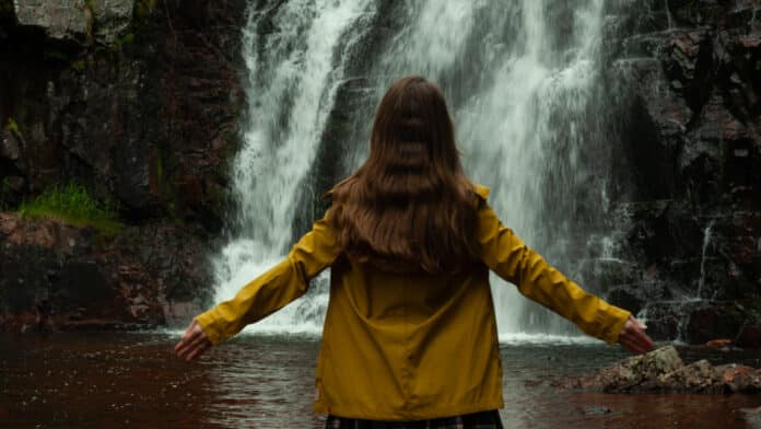 Lisah Silfwer in a yellow raincoat in front of a waterfall.